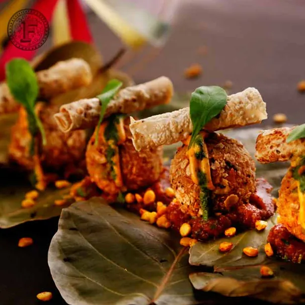 Dal chawal arancini on a leaf, each topped with a rolled papad and a micro-green, with crispy corn