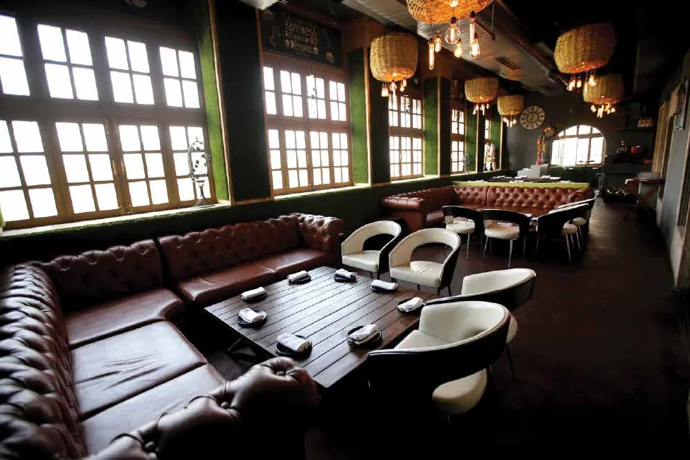 Farzi Cafe lounge with tufted brown leather sofas, white tub chairs, tall paned windows and woven basket pendant lights
