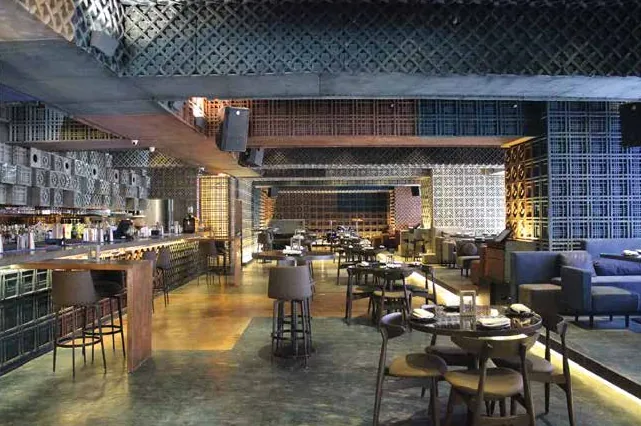 Industrial-style dining hall with lattice ceiling, bar seating and warm floor lighting