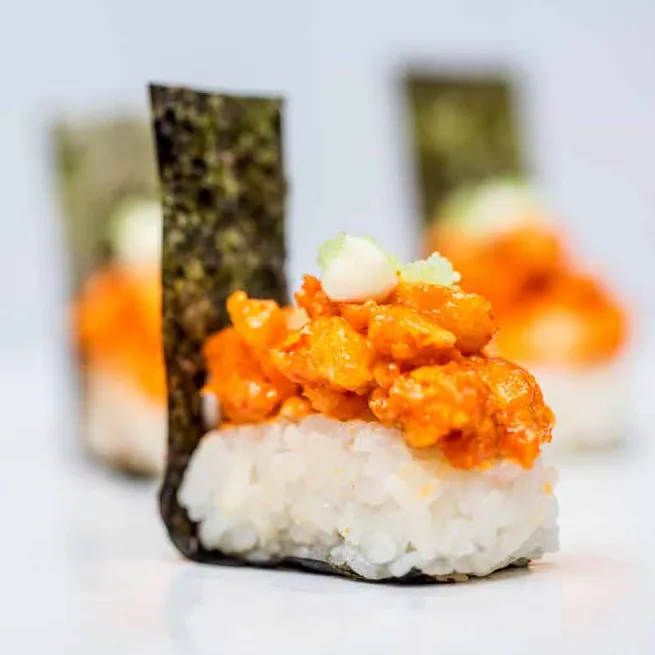 Nori-wrapped rice topped with spicy orange seafood, shot with shallow depth of field