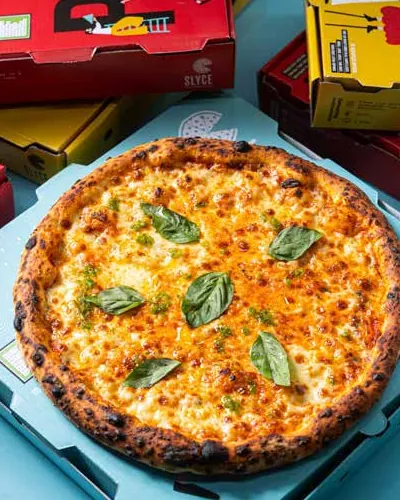 Golden cheese pizza with basil leaves on a light-blue box