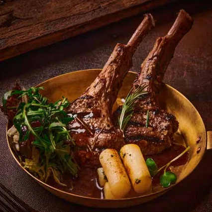 Grilled lamb chops in a brass bowl with pepper jus, greens and roasted potatoes