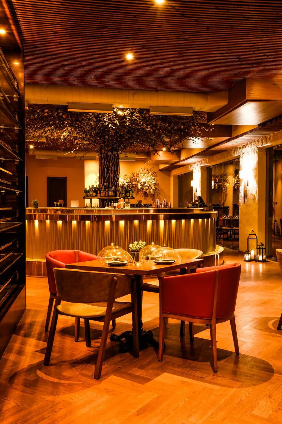 Swan's warmly lit bar and dining room, with a sculptural tree canopy over a curved gold bar and red chairs